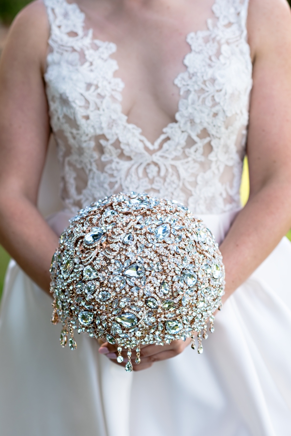A bride in a lace wedding dress holding a bouquet made of jewels.